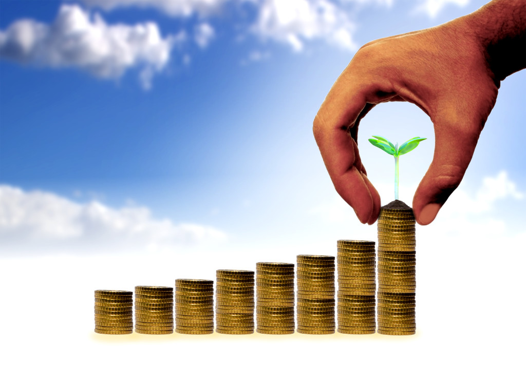 Businessman adding golden coins with a young plant in the final row of a coin stack - Money and financial assets growth concept